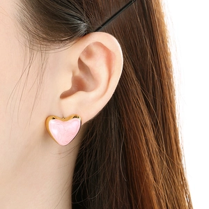 Pink heart-shaped enamel earrings with gold marble texture on female model ear