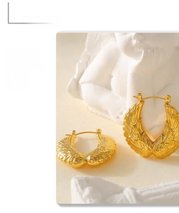 Detail shot of golden wing textured hoop earrings displayed on a white statue base