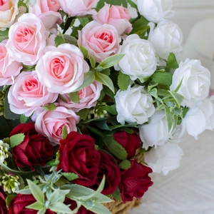 Detail of colorful artificial silk roses in pink, white and red inside a woven basket