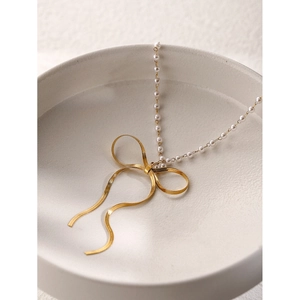 Elegant 18k gold butterfly bow pendant necklace with white pearls in a ceramic bowl