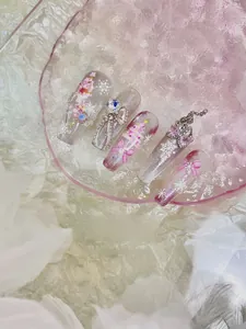 Close-up of pink glitter press-on nails with white snowflakes and 3D bow charms