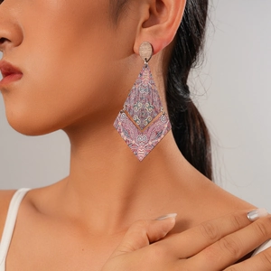 Close-up of geometric wooden earrings with pink and grey ethnic patterns on a female model