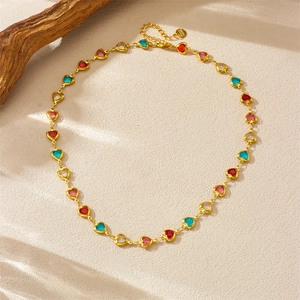 Golden necklace with colorful heart-shaped rhinestones on textured beige surface