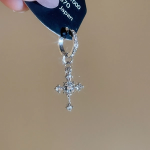 Macro shot of silver cross hoop earring with sparkling zircons and a punk vintage finish
