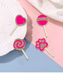 Detail of four pink cat paw and lollipop enamel brooches with gold frames and rhinestones