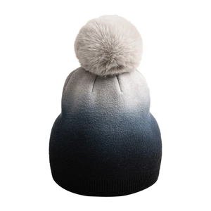 Detail einer Strickmütze mit Farbverlauf und einem flauschigen Bommel für den Winter