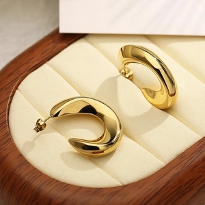Minimalistische C-vormige oorringen verguld met 18k goud op een houten sieradendoos