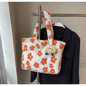 Detail of white plush tote bag with orange floral patterns and a cute doll pendant