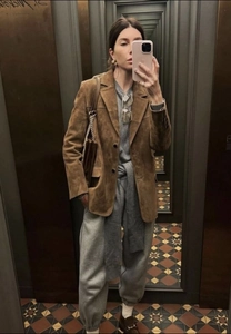 Chic detail of a brown suede blazer paired with a grey tracksuit and chain handbag
