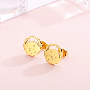 Close-up of golden round stud earrings featuring engraved sun and star celestial patterns