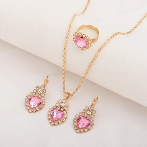 Detailed view of gold jewelry set featuring pink heart crystals on white fabric background