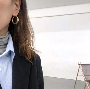Close-up of golden hollow hoop earrings in titanium steel worn by a fashion model
