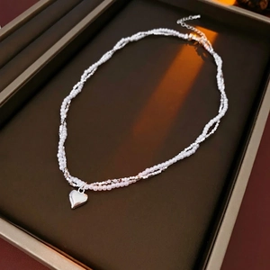 Elegant double-layer pearl necklace with silver heart pendant on brown leather tray