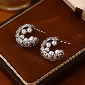 Macro shot of silver C-shaped earrings with sparkling cubic zirconia and inner pearls