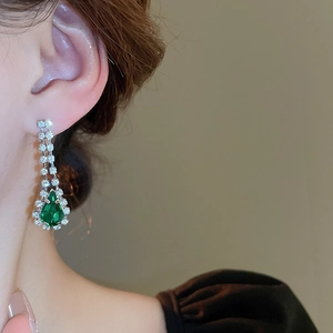 Detail of drop tassel earrings with green teardrop stones and rhinestone accents
