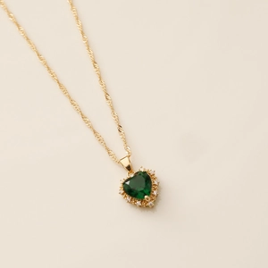 Detail of emerald green heart pendant with crystal halo on gold-tone twist chain necklace
