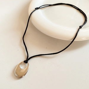 Close-up of a silver oval cutout pendant with a minimalist black adjustable cord