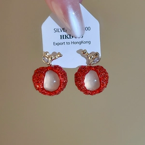 Close-up of sweet apple-shaped earrings with red resin and gold leaf details