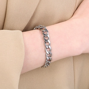 Close-up of a silver Cuban link bracelet worn with a beige suit jacket for daily style