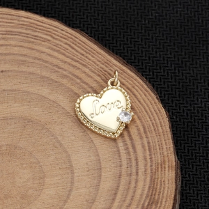 Dettaglio di un ciondolo a cuore dorato con incisione Love e una gemma scintillante
