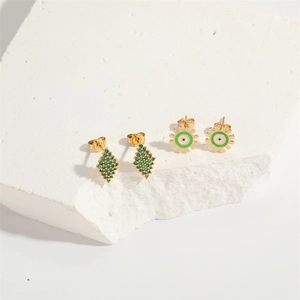 Detail of gold gear earrings with green zircon and enamel on white textured stone