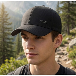 Detail of a black baseball cap with a silver signature logo on a blurred forest background