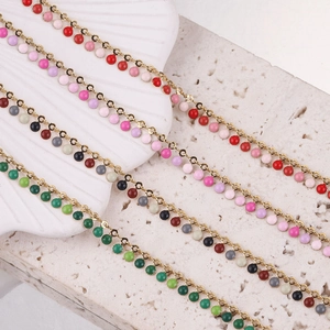 Detailed view of colorful enamel bead chains on a textured stone with a white seashell