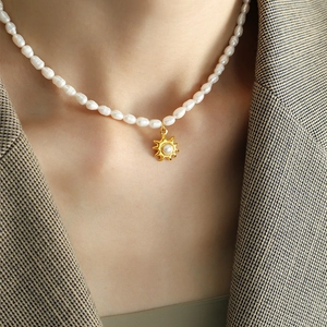 Elegant freshwater pearl necklace with gold sun pendant worn on a herringbone blazer