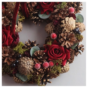 Close-up of Christmas wreath with red roses, pine cones, and velvet ribbon detail