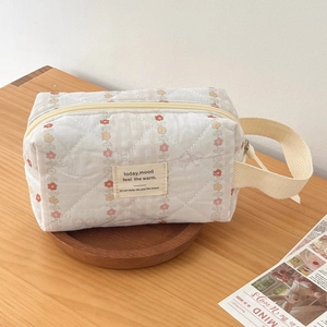 Floral quilted cosmetic bag with red and yellow flower patterns on a wooden tray