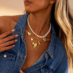 Detail of layered gold chain and white pearl necklace with 3D heart pendants