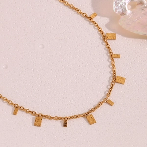 Detail of 18K gold plated square pendants on a thin chain over wet pink texture