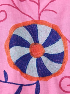 Detailed close-up of colorful floral embroidery on breathable pink linen fabric