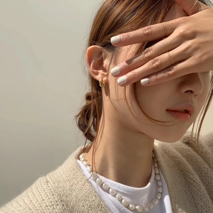 Close-up of minimalist gold twisted hoop earrings and pearl necklace on a model