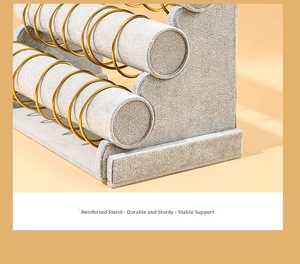 Close-up of a three-tier gray velvet jewelry stand showcasing golden metal bracelets