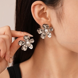 Macro detail of silver flower petal earrings with pearl center and metallic texture