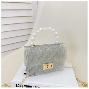 Detail of glitter jelly bag with pearl handle and golden chain on a white book
