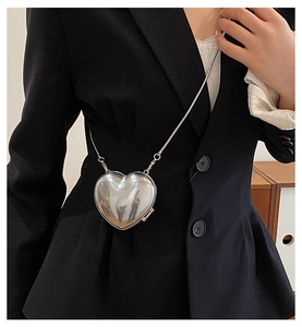 Close-up of heart-shaped silver metallic mini bag with snake chain worn on a black blazer