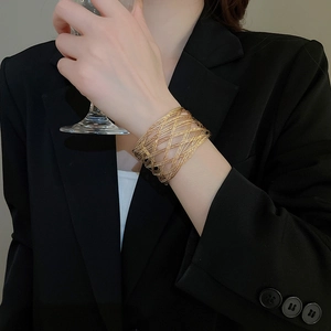 Close-up of a wide gold woven mesh bracelet with intricate hollow layered texture