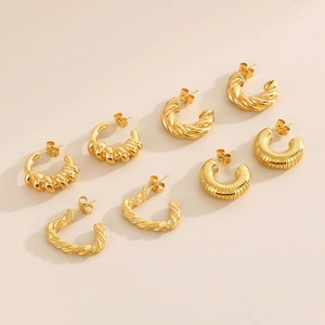 Détail de plusieurs boucles d'oreilles créoles en C en acier titane doré sur fond beige