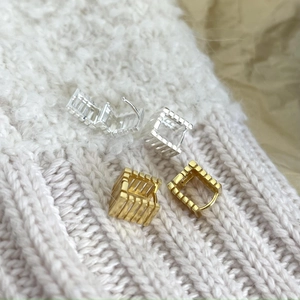 Macro view of geometric square hoop earrings in gold and silver on knit fabric