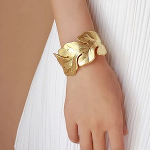 Detail of golden leaf-shaped cuff bracelet with brushed metal texture and adjustable open design