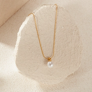 Close-up of golden stainless steel necklace with a lustrous white pearl on stone background