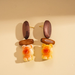 Detail of wooden geometric earrings with amber resin bear charms and gold needles