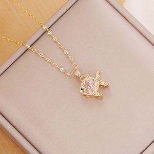 Detail shot of a gold fish pendant with zircon inlay on a beige jewelry box