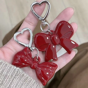 Close-up of two red acrylic bow keychains with heart-shaped metal rings held in hand