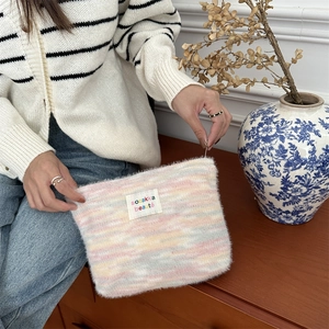 Macro view of rainbow plush toiletry bag featuring soft striped fur and brand logo label