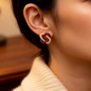 Close-up of elegant double-loop intertwined earrings with red enamel and zircons