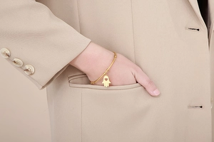 Close-up of a gold Hamsa hand charm bracelet with heart cutout on a female model