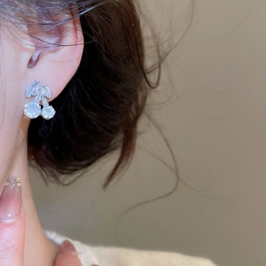 Close-up of zircon-inlaid cherry stud earrings worn by a model in a warm setting